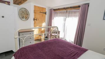 Un dormitorio con cama, cómoda, silla, puerta de madera y ventana con cortinas.