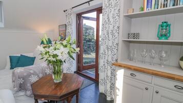 Un salón acogedor con una mesa de madera, un jarrón de flores, un sofá con cojines color turquesa y una estantería con libros y objetos decorativos.