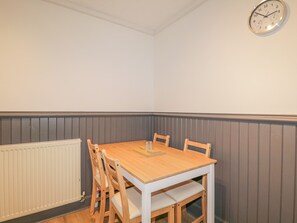 Ein Eckzimmer mit Holztisch und vier Stühlen, einem weißen Heizkörper und einer Wanduhr.