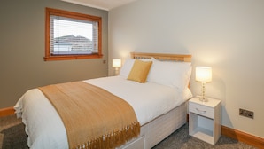 Una cama bien hecha con cabecera de madera, dos lámparas de noche y una ventana con persianas.