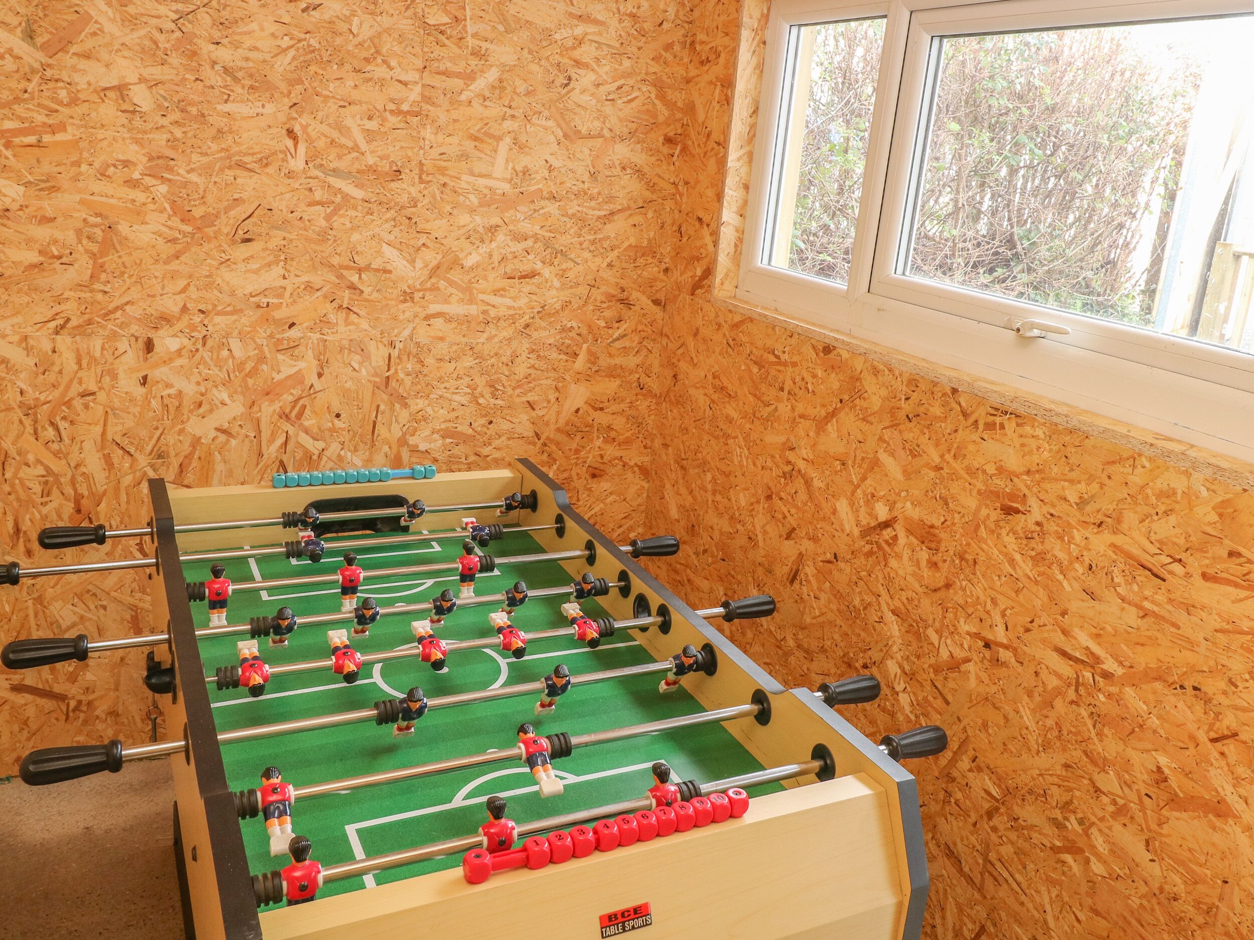 Una mesa de fútbolín en una habitación con paredes de madera y una ventana.