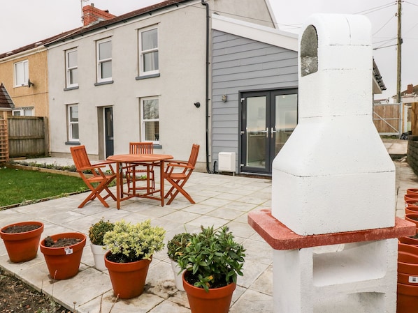 A patio with a barbecue grill, a table with chairs, and potted plants.