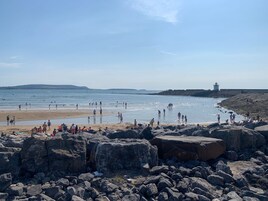 A rocky beach with people enjoying the water and the view of a lighthouse in the distance.
