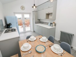 A modern kitchen with a gas stove, a coffee machine, and a dining area set for four with white plates and glasses.