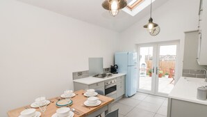 A modern kitchen with a dining table set for four, a blue refrigerator, and a view of the backyard through a glass door.