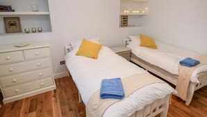 A bedroom with two single beds, a dresser, a mirror, and a shelf with books and decorative items.
