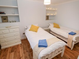 A bedroom with two single beds, a dresser, a mirror, and a shelf with books and decorative items.