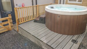 A wooden deck with a hot tub, a wooden fence, and a door.