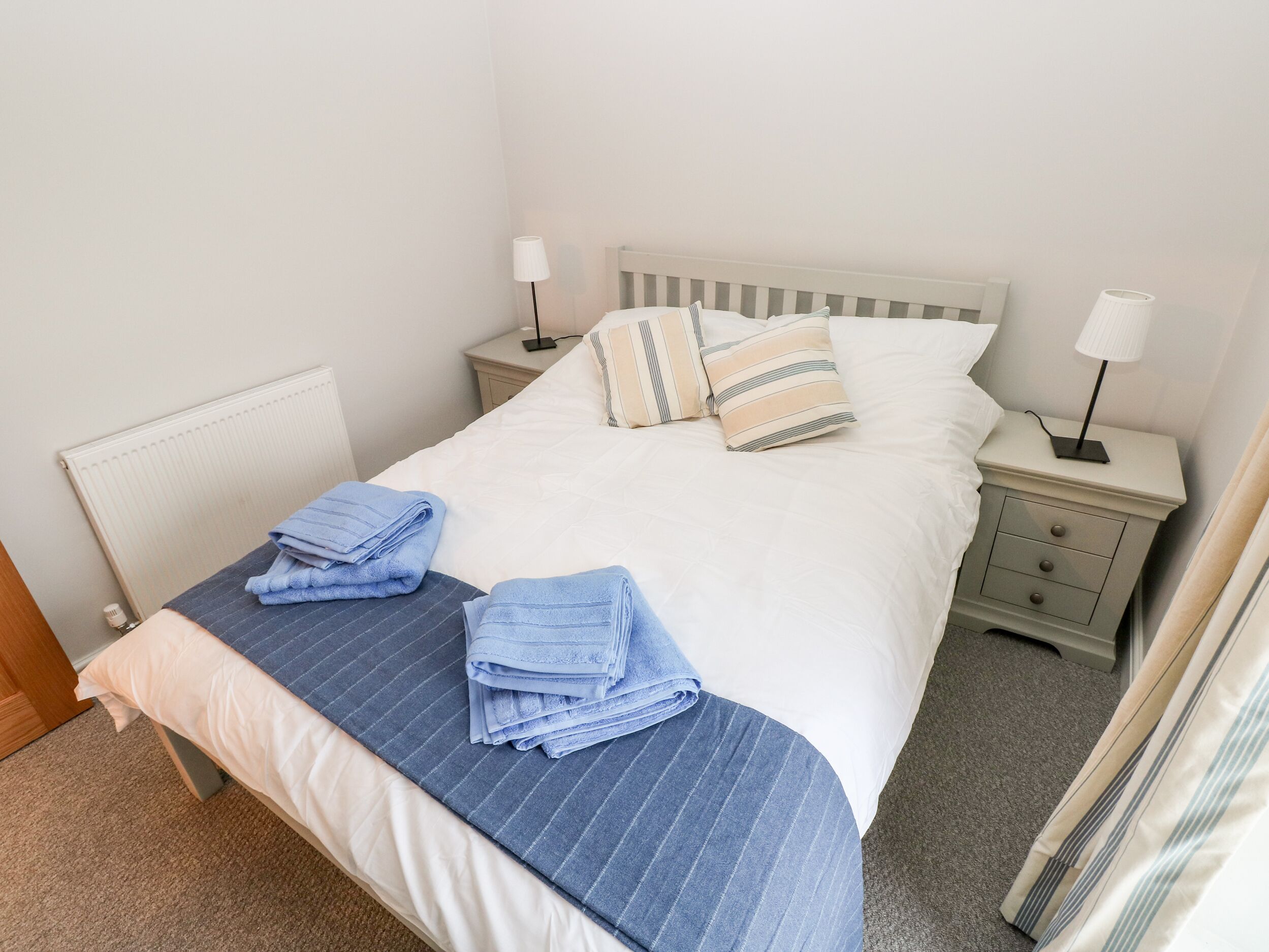 A neatly made bed with blue and white linens, two bedside lamps, and striped pillows.
