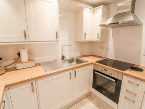 A modern kitchen with white cabinets, a stainless steel sink, a Bosch oven, and a black induction cooktop. - Pearsall (Ambleside)