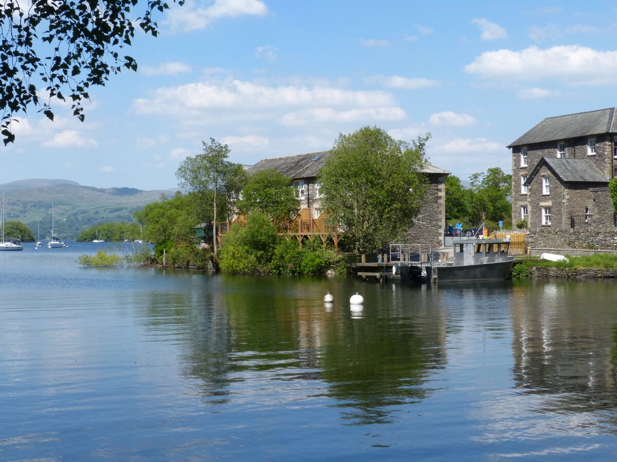 A riverside hotel with stone buildings, a dock, and boats in the background.