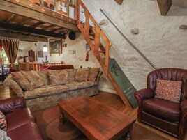 Una sala acogedora con una escalera de madera, un sillón de cuero, un sofá floral y una mesa de centro de madera.