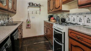 A kitchen with wooden cabinets, a gas stove, an oven, and a hanging pot rack.