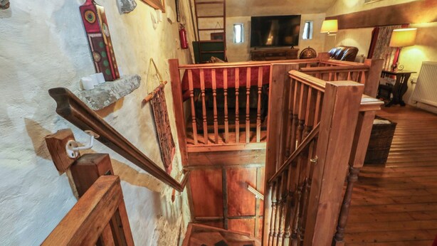 A wooden staircase with a handrail, a fire extinguisher, and a television in the background.