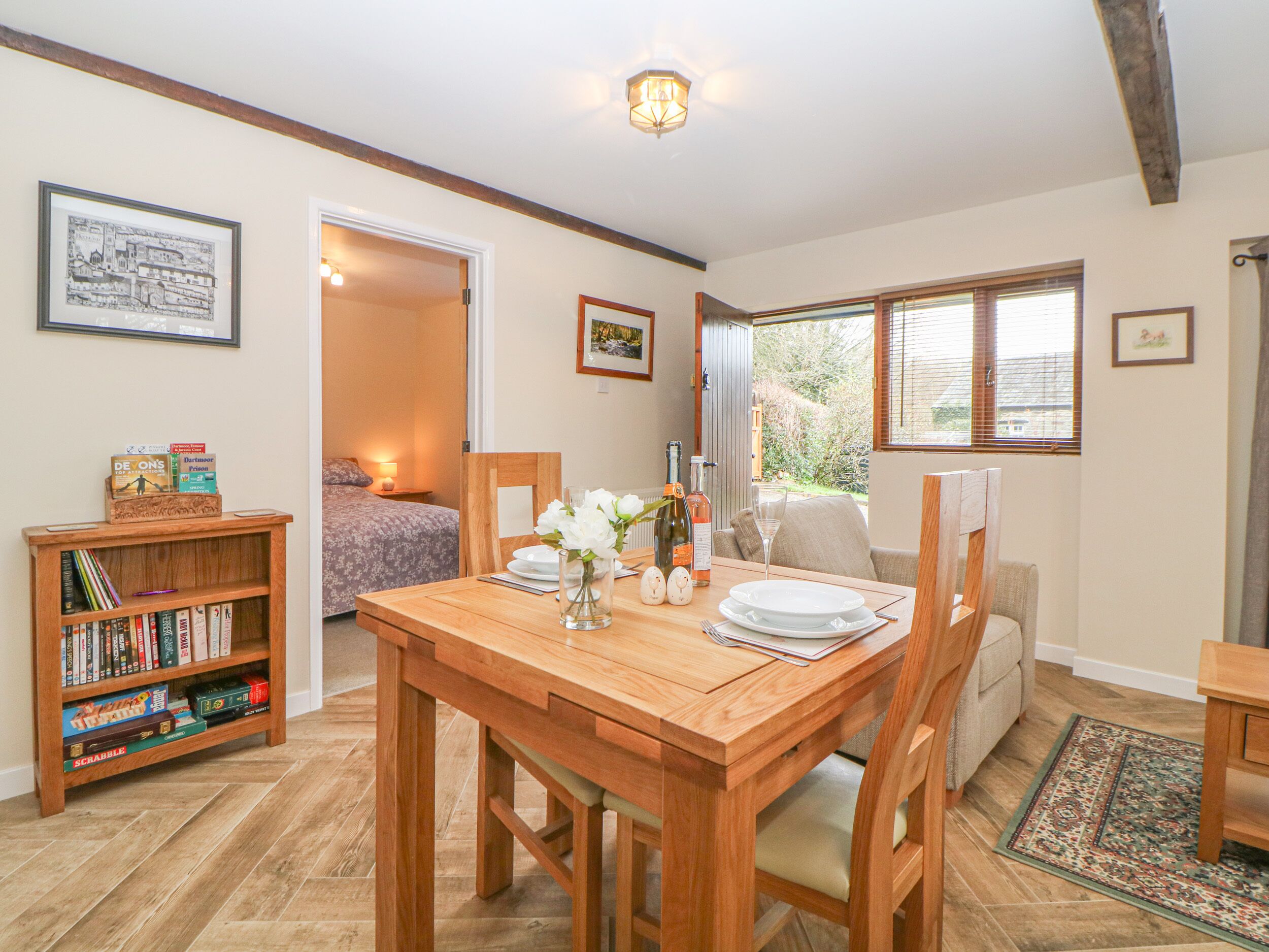 Una habitación acogedora con una mesa de madera, sillas, una estantería y una cama.