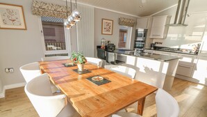 Una cocina moderna con armarios blancos, electrodomésticos de acero inoxidable y una mesa de comedor de madera con sillas blancas.