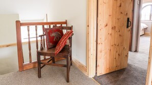 A wooden chair with a red cushion and a patterned pillow in a room with a wooden door and a carpeted floor.