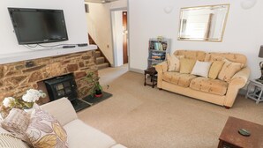 A living room with a stone fireplace, a beige sofa, a television mounted on the wall, and a bookshelf.
