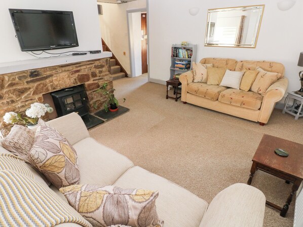 A living room with a stone fireplace, a beige sofa, a television mounted on the wall, and a bookshelf.