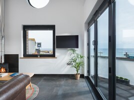 Una sala de estar moderna con un ventanal grande, un televisor de pantalla plana, una planta en maceta y una chimenea.