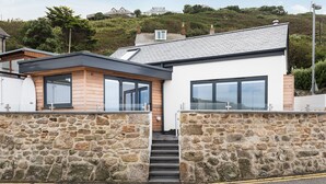A modern house with a stone wall entrance, large windows, and a staircase leading to the door.