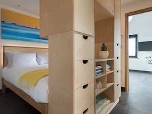 A modern bedroom with a bed, a wooden wardrobe, and a painting on the wall. - The Old Beach Store (Penzance)