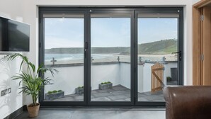 A modern living room with a large sliding glass door leading to a balcony overlooking a beach.