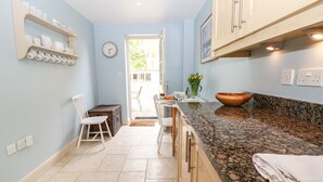 A kitchen with light blue walls, a granite countertop, and wooden cabinets. There is a clock on the wall, a window, and a door leading outside.