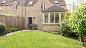 A stone house with a sloped roof, a front door, and a small patio with a table and chairs.
