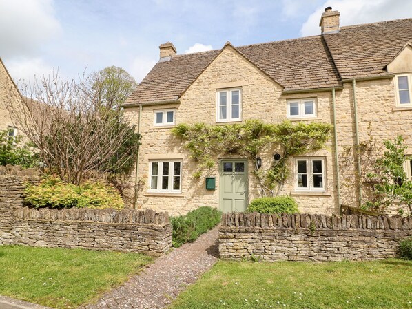 A stone house with a green door, multiple windows, and a stone wall in front. - 3 Painters Field (Cirencester)