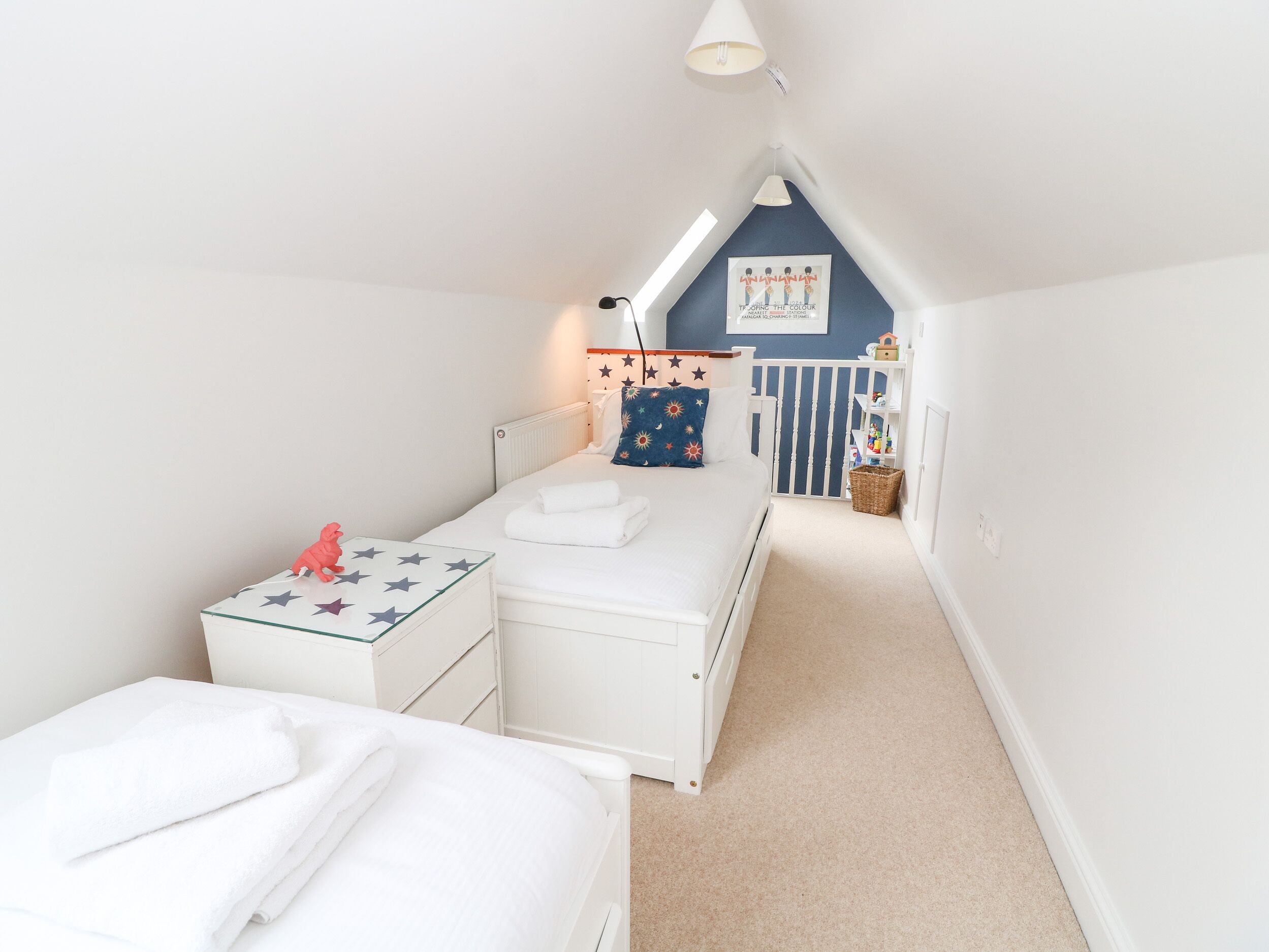 A small, well-lit attic bedroom with two beds, a white dresser, a star-patterned table, and a ceiling light.