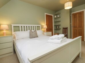 A neatly made bed with white linens, two bedside lamps, and a wooden headboard. - 3 Painters Field (Cirencester)