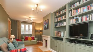 A cozy living room with a green sofa, a red plaid throw blanket, a fireplace, and a bookshelf filled with books.