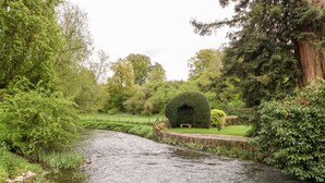 A river flowing through a park with lush greenery and a round hedge.