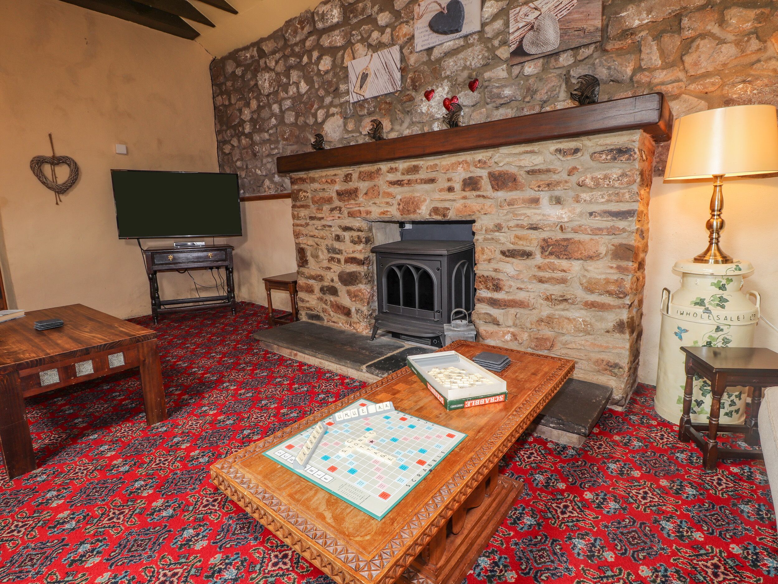 A cozy room with a stone wall, a fireplace, a wooden table with a board game, a television, and a lamp.