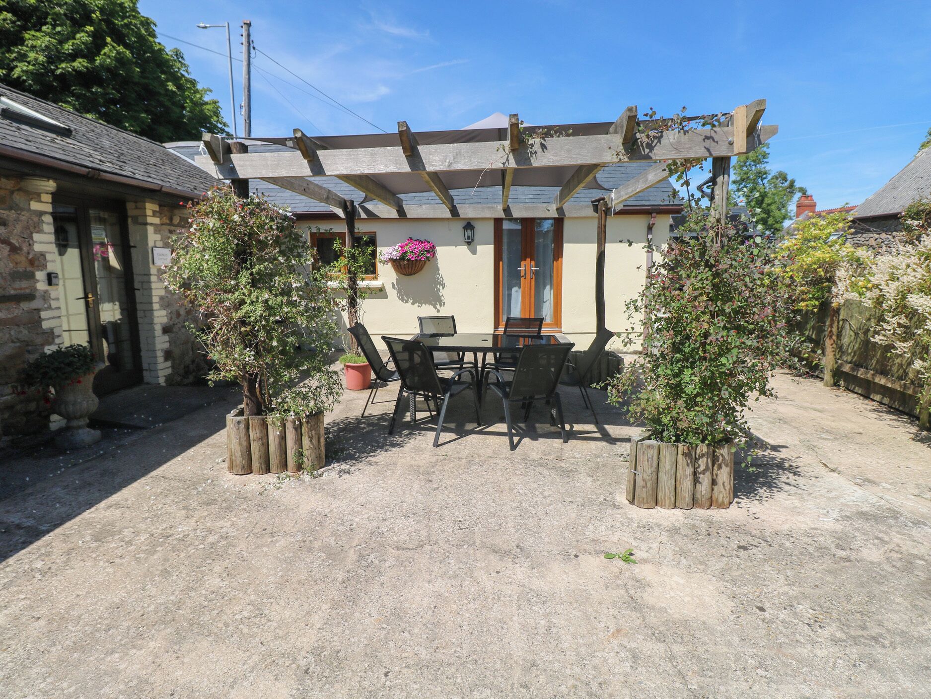 A covered patio with a table and chairs, surrounded by potted plants.