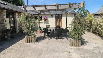 En overdækket terrasse med bord og stole, omgivet af krukker med planter.