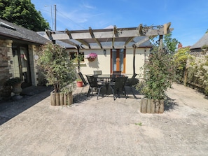 A covered patio with a table and chairs, surrounded by potted plants. - Stoney Cottage (Narberth)