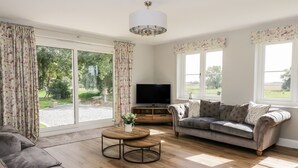 A living room with a grey sofa, a round coffee table, and a flat-screen TV. - West Farm (Great Yarmouth)