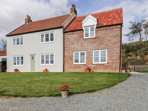 A two-story house with a red-tiled roof, a brick section, and a white section. There are potted plants with red flowers in front of the house. - West Farm (Great Yarmouth)