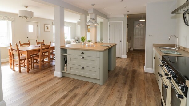 A modern kitchen with wooden flooring, a central island, and a built-in oven. - West Farm (Great Yarmouth)