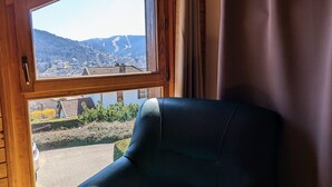Een kamer met een groot raam, met uitzicht op een bergachtig landschap en een stad daaronder.