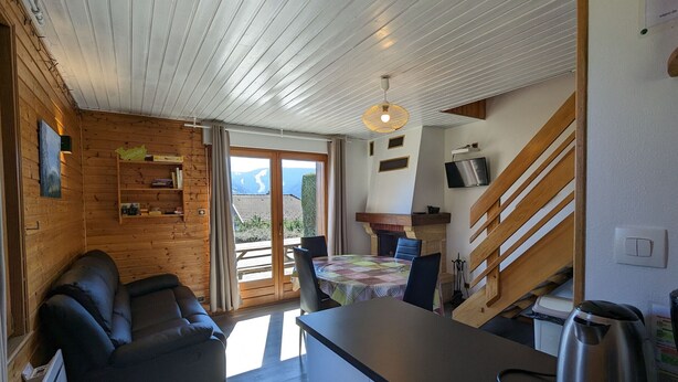 Een gezellige keuken met een houten plafond, een eethoek met een tafel en stoelen, een bank en uitzicht op de bergen door de schuifpui.