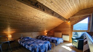 Een gezellig zolderkamer met houten wanden en schuine plafonds, met twee bedden, een stoel en een groot raam met een prachtig uitzicht.