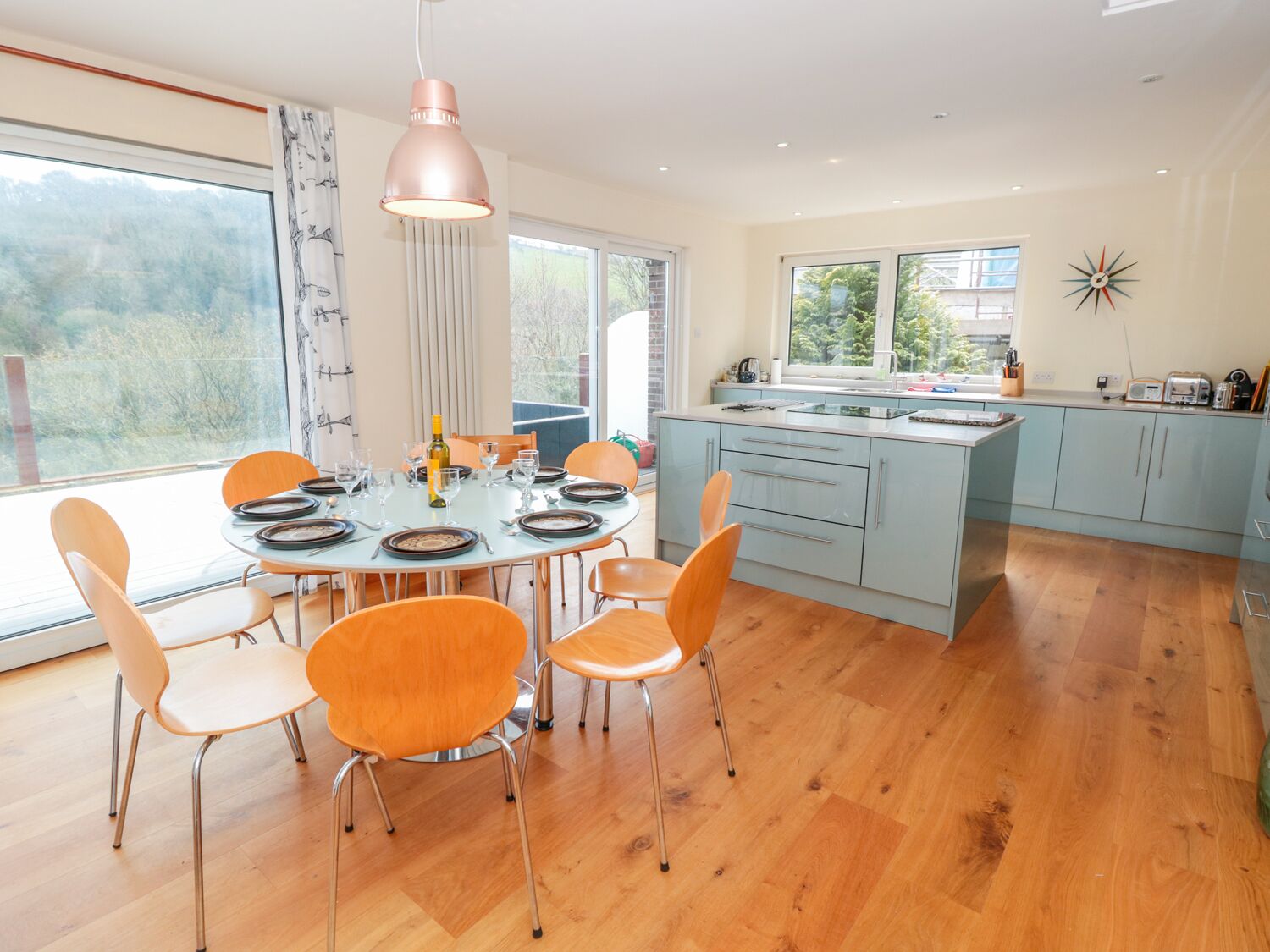 A modern kitchen with a round dining table, orange chairs, and a pendant light.