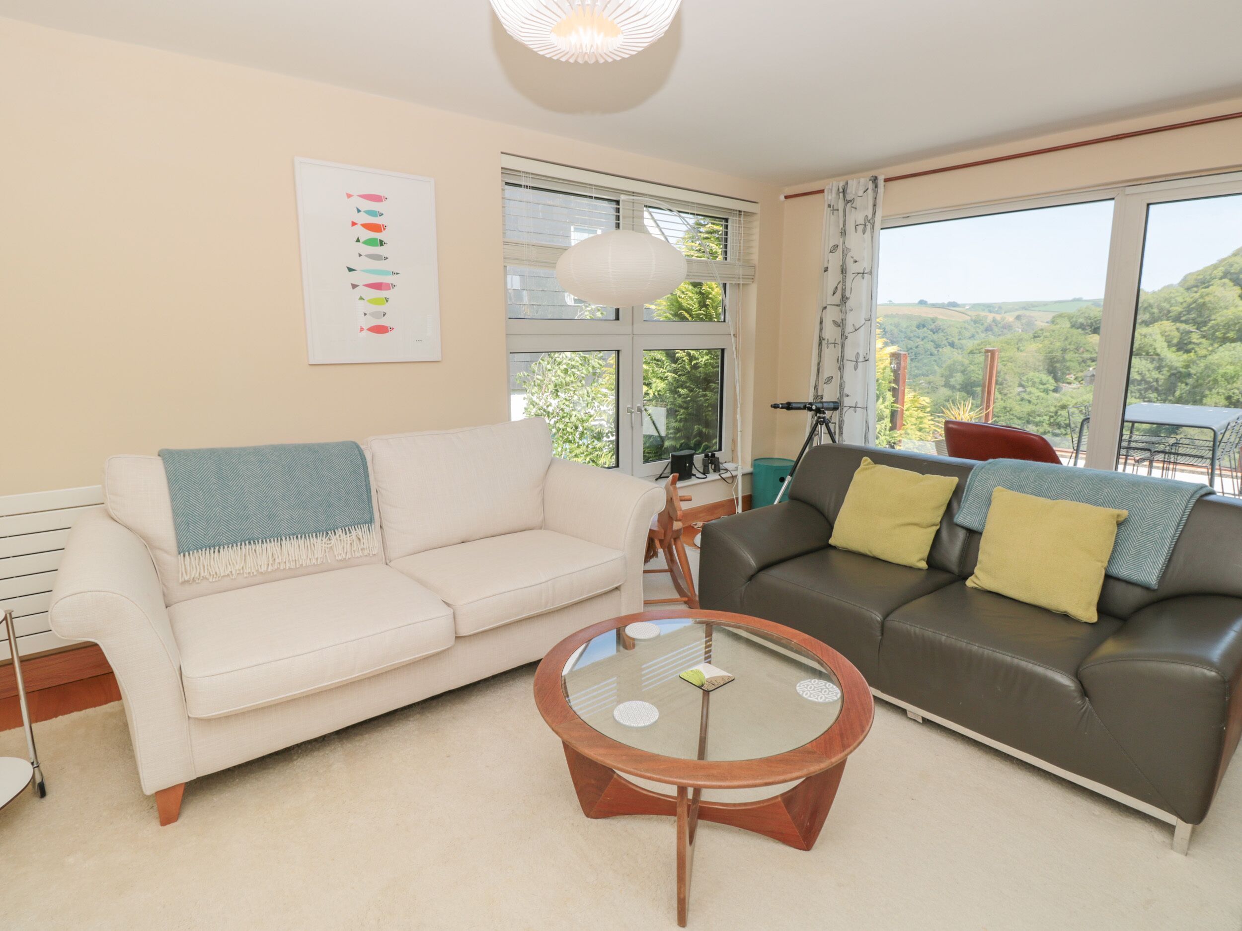 A living room with two sofas, a glass coffee table, and large windows offering a view of greenery.
