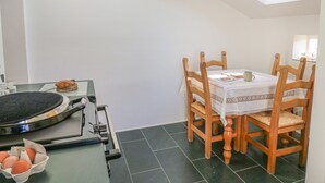 Uma sala de jantar com uma mesa posta para quatro pessoas, cadeiras de madeira, um ventilador de teto e um claraboia.