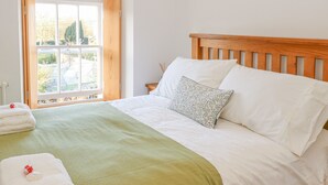 Cama bem arrumada com manta verde, lençóis brancos e almofada estampada com flores.