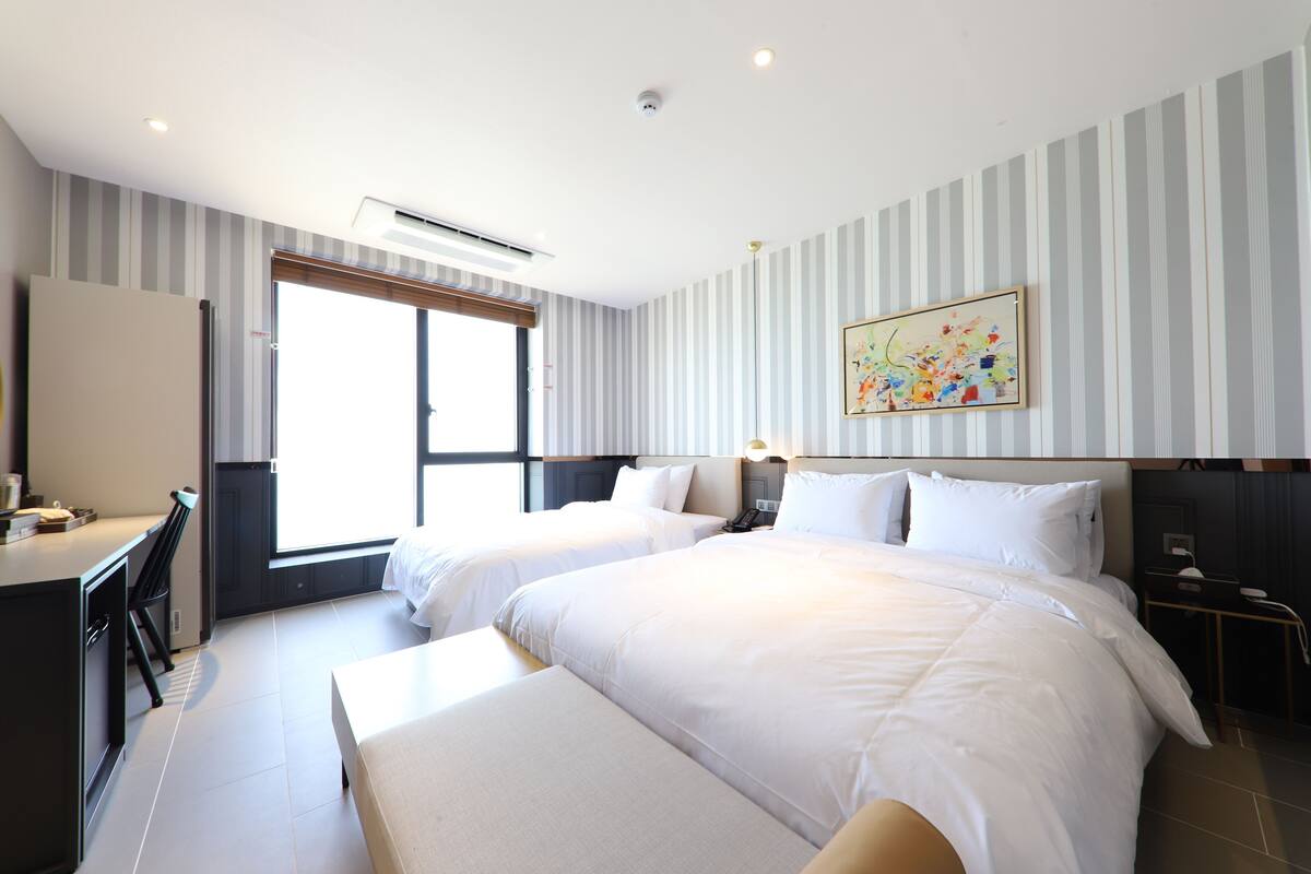 Habitación de hotel con dos camas, un escritorio y una ventana con persianas.