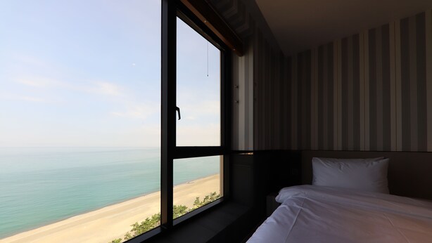 Une chambre d’hôtel dotée d’une grande fenêtre donnant sur la plage et l’océan.